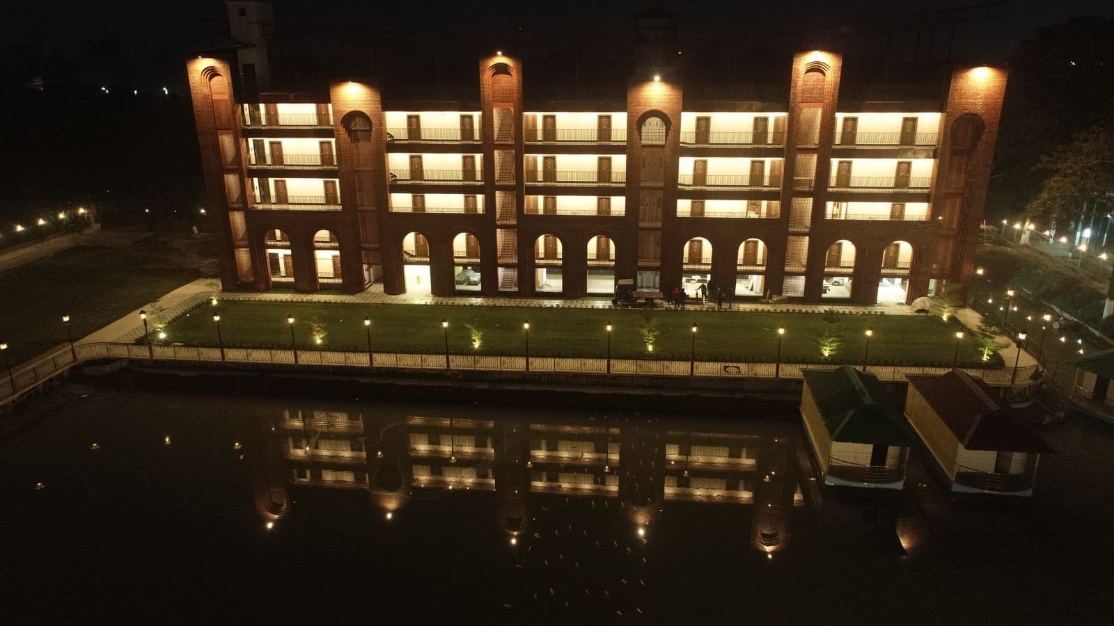 The lit brick arcade of Mahfil-e-Motijheel reflected in the water at dusk